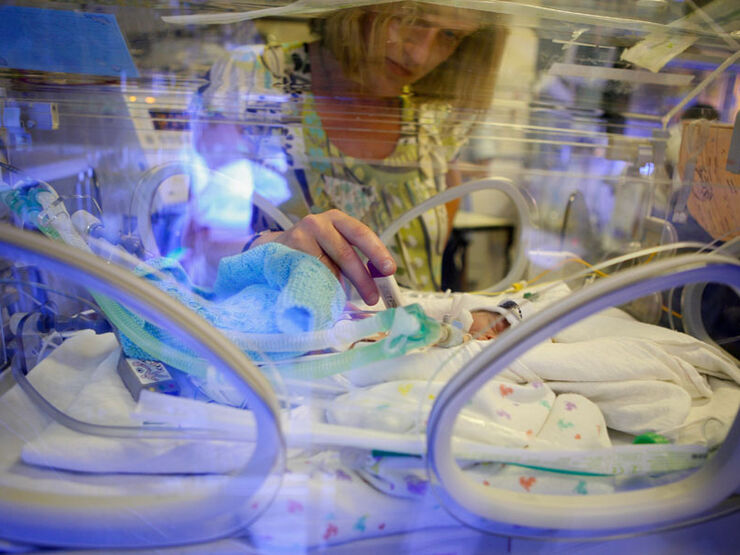 Mum touching her premature baby through an incubator