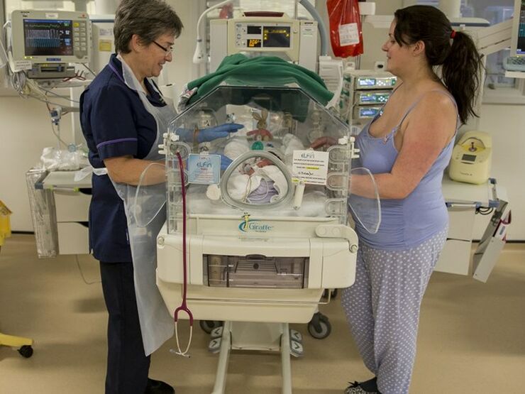 Mum and nurse with their hands through an incubator touching a baby