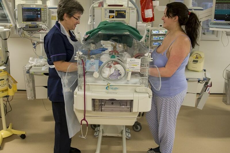 Mum and nurse with their hands through an incubator touching a baby