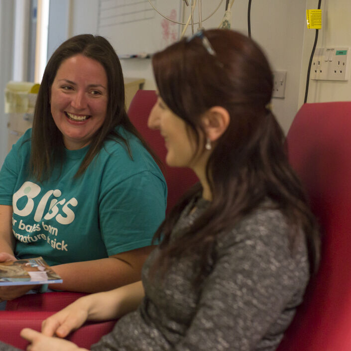 Recent mum and Bliss volunteer sat on hospital chairs talking and laughing