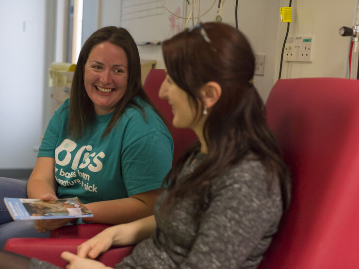 Recent mum and Bliss volunteer sat on hospital chairs talking and laughing