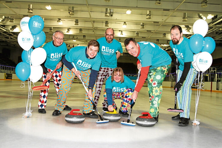 six people in Bliss t-shirts and colourful trousers with their curling equipment and Bliss balloons
