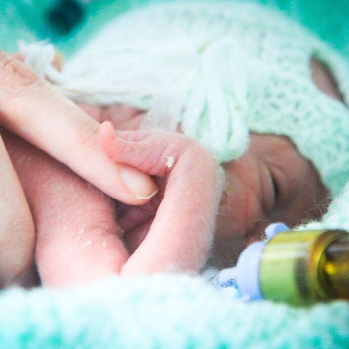 Premature baby attached to a tube with their parent's hand on them