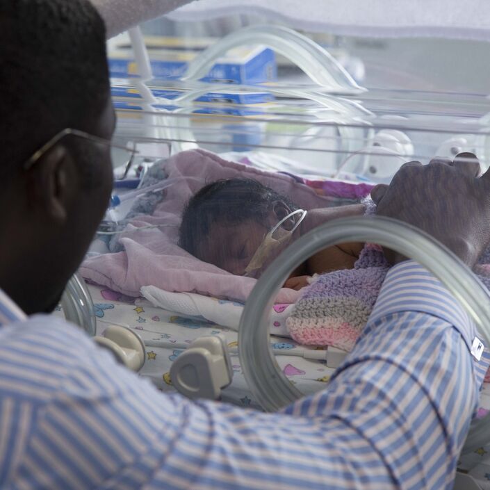 Dad in hospital reaching his hand into an incubator to touch his baby.