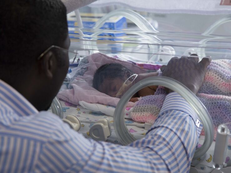 Dad in hospital reaching his hand into an incubator to touch his baby.