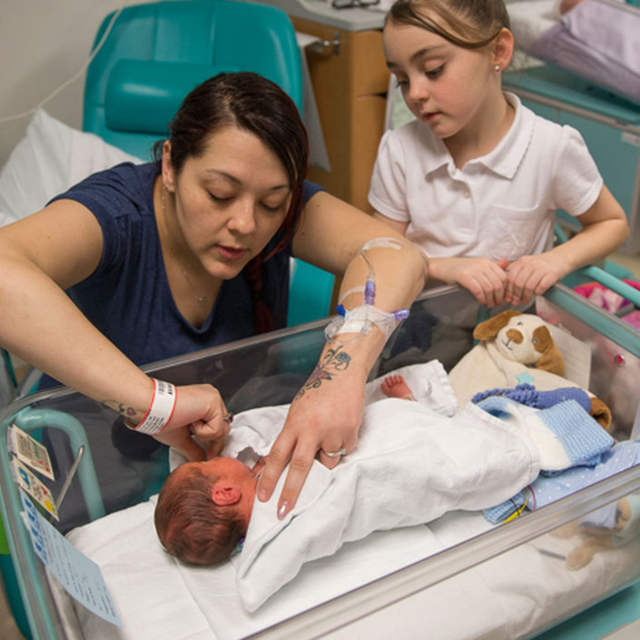 Mum helping baby in cot with big sister looking on