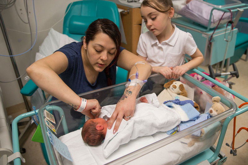 Mum helping baby in cot with big sister looking on