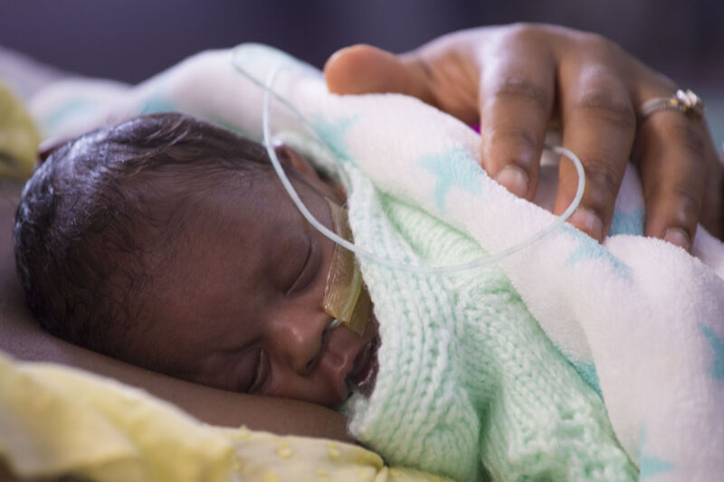 Premature baby wrapped in blanket sleeping on parent's chest with parent's hand on baby's back