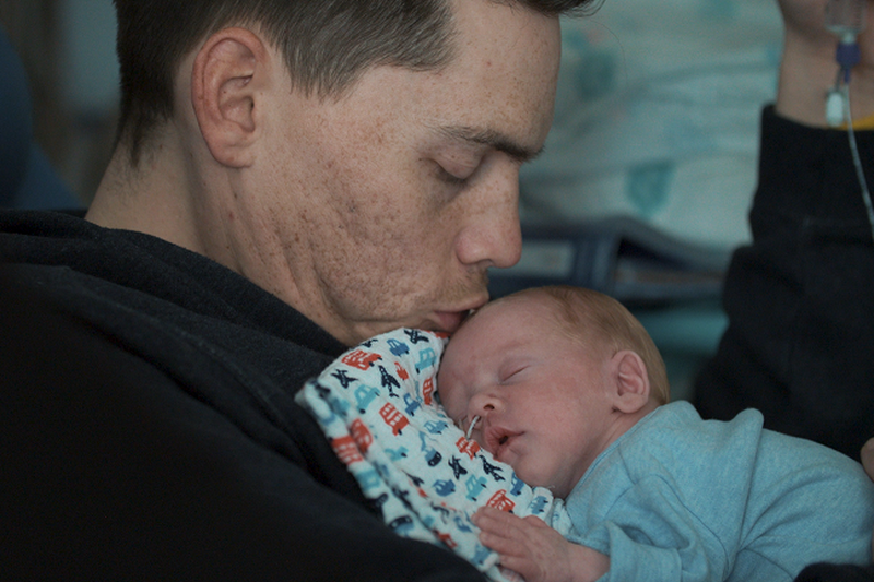 Dad holding his premature baby on his chest while he kisses baby's head