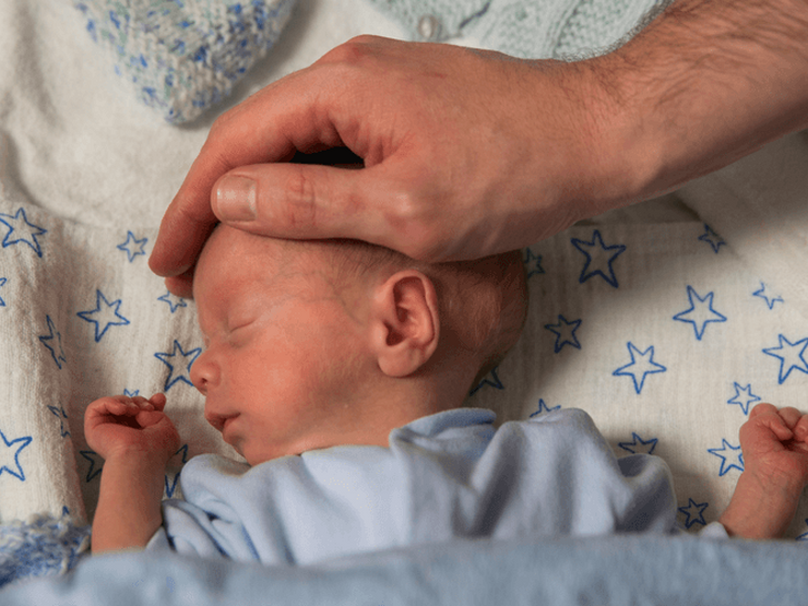 Parent placing hand on baby's head while baby sleeps peacefully