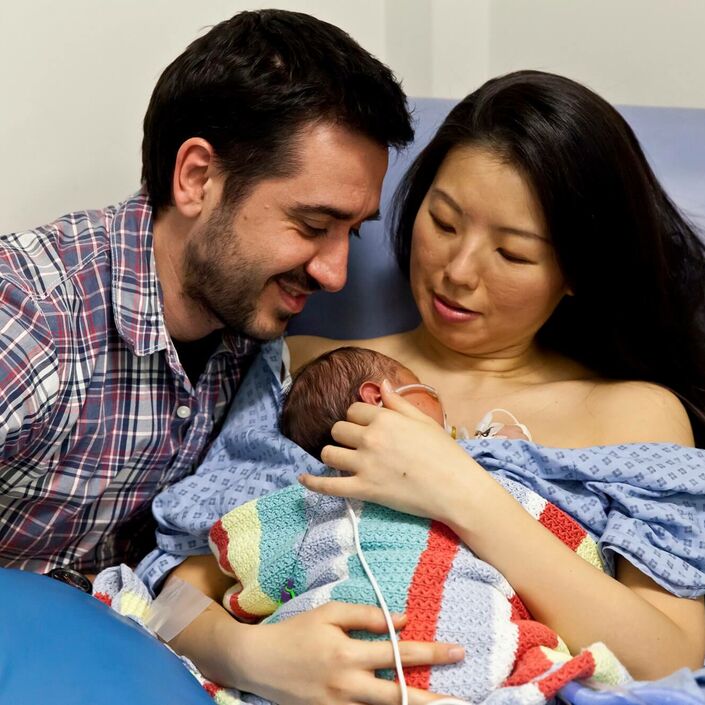 Mum and dad sat together with mum holding baby on her chest