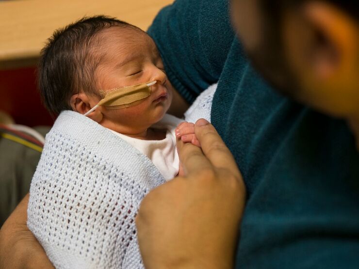Dad holding baby wrapped in blanket attached to feeding tube