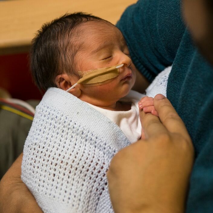 Dad holding baby wrapped in blanket attached to feeding tube