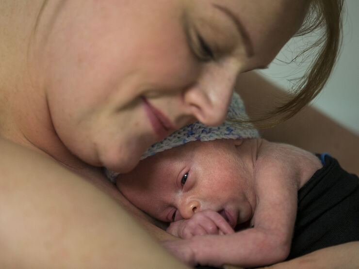 Baby cuddling on mum's chest skin to skin with mum leaning her head down towards baby and smiling