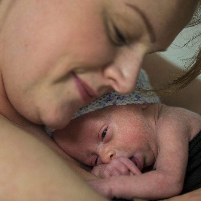 Baby cuddling on mum's chest skin to skin with mum leaning her head down towards baby and smiling