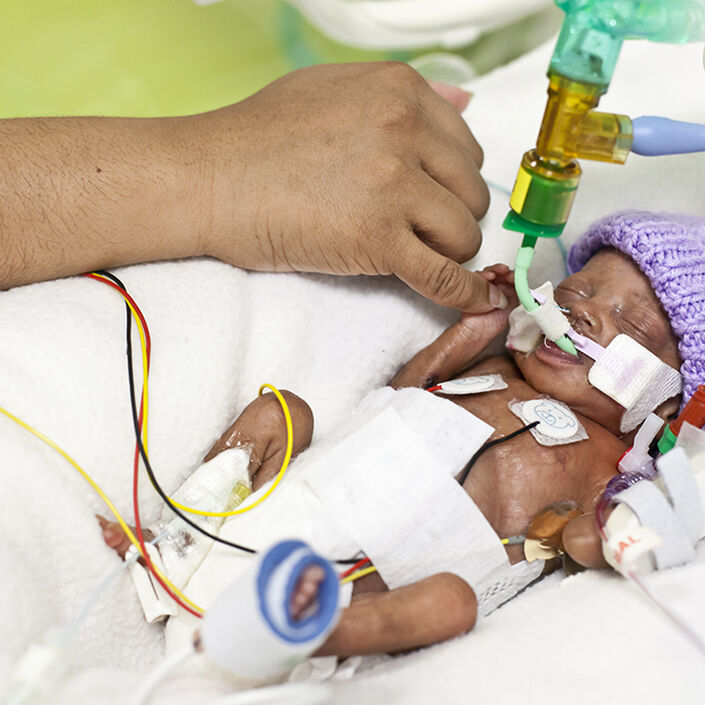 Baby in cot holding onto parent's finger