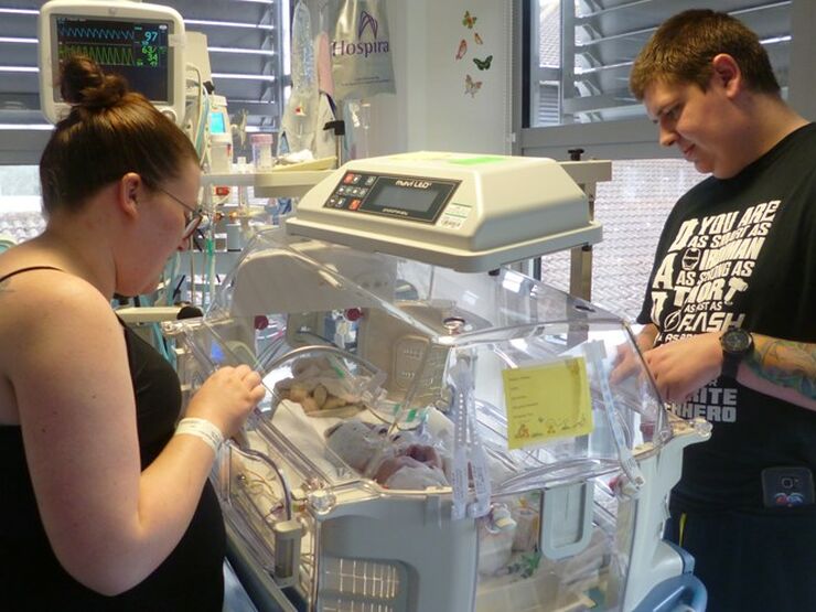 Mum and dad standing at either side of an incubator looking down at their newborn baby