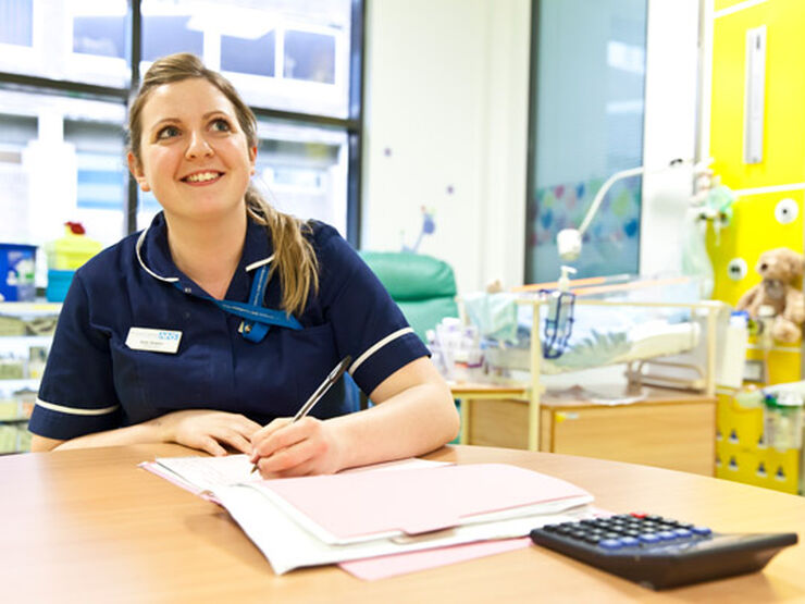 Nurse doing paperwork sitting at a desk looking up and smiling