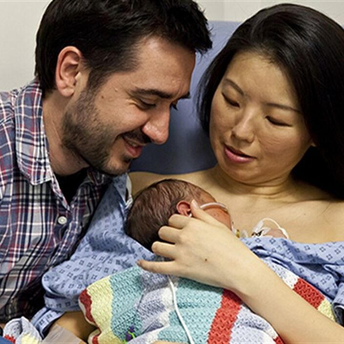 Mum in a hospital gown with baby resting on chest skin to skin and dad kneeling beside them