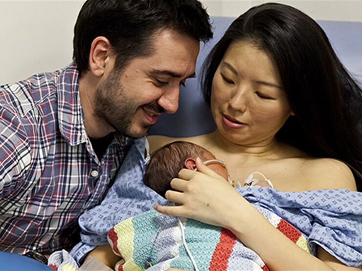 Mum in a hospital gown with baby resting on chest skin to skin and dad kneeling beside them