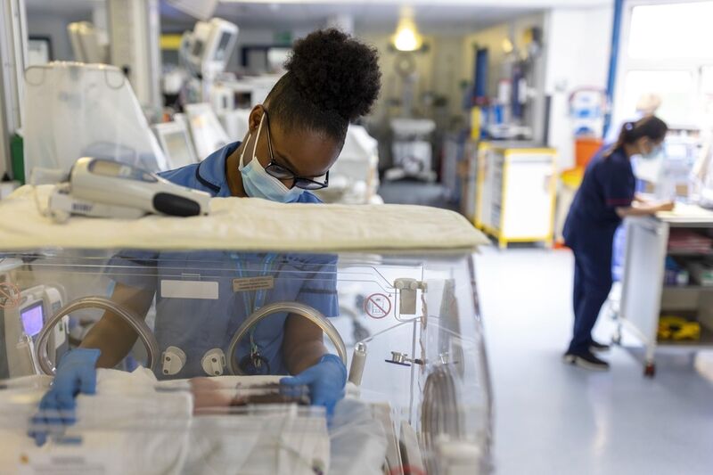 A nurse with her hands inside an incubator where there is a baby wrapped in a white blanket.