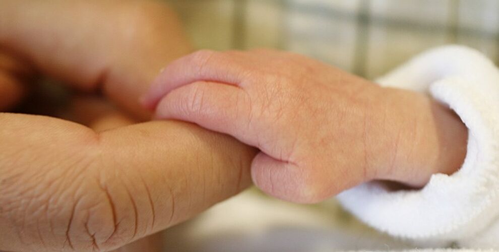 Close up of baby's hand holding the finger of a parent