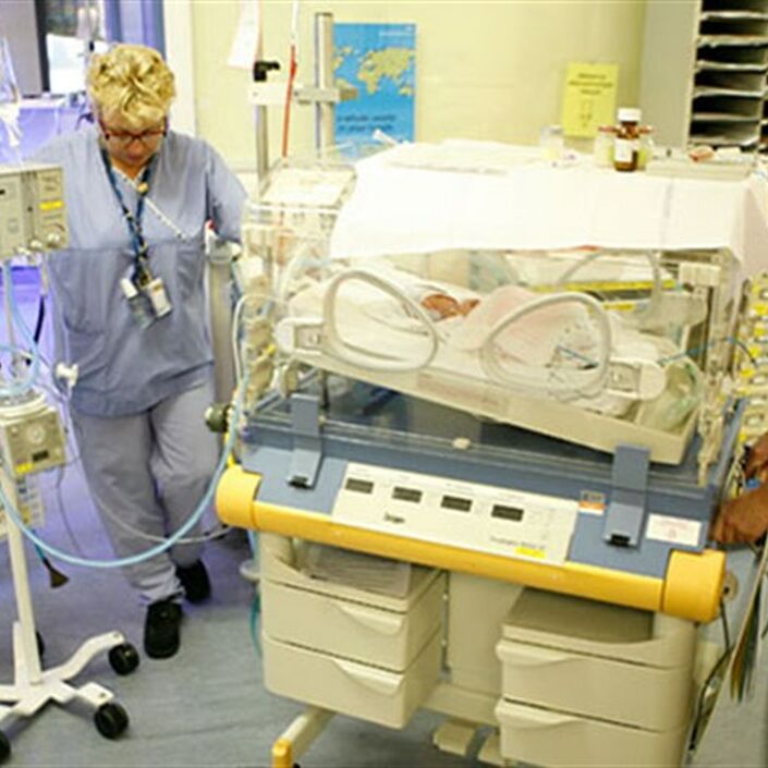 Two medical staff pushing a cot in hospital to transfer a baby