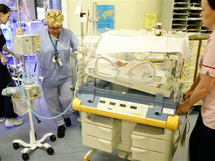 Two medical staff pushing a cot in hospital to transfer a baby