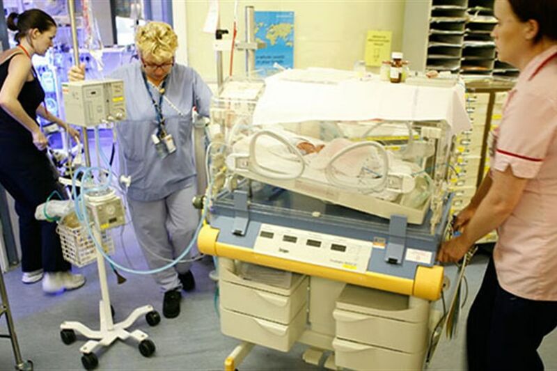 Two medical staff pushing a cot in hospital to transfer a baby