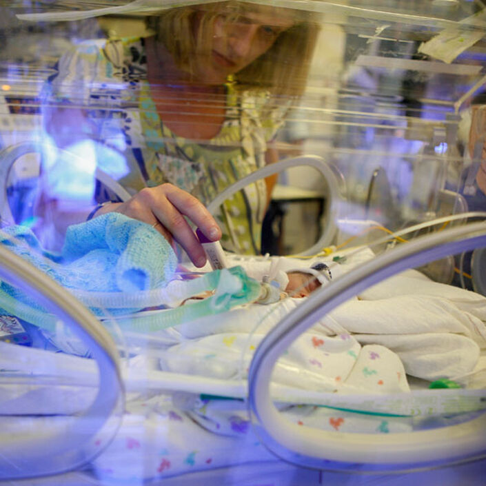 Mum holding hands with baby in incubator