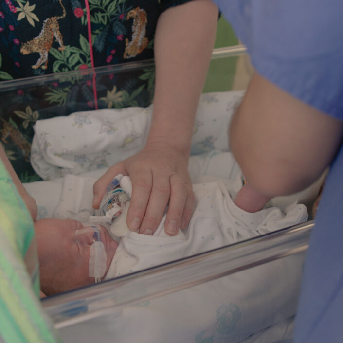 Parent touching their baby who is asleep in a hospital cot