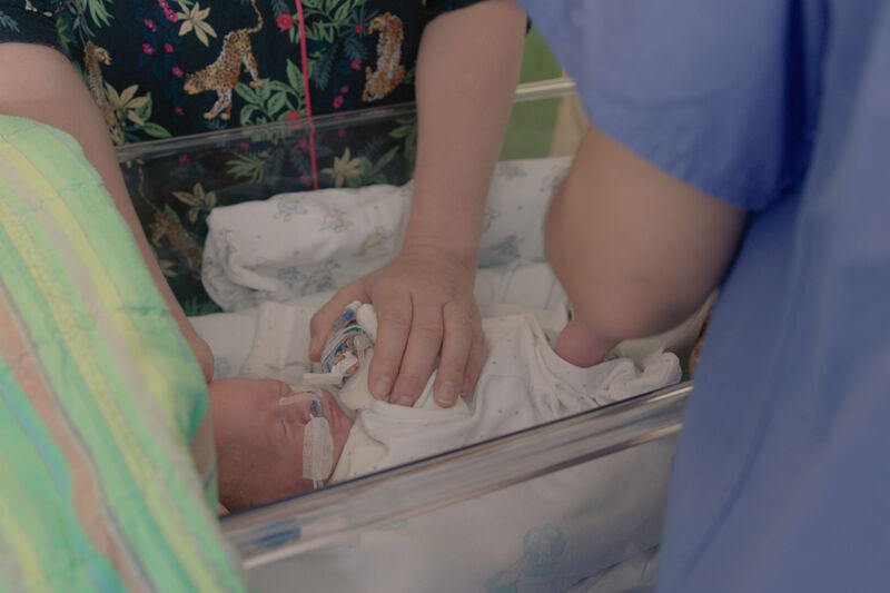 Parent touching their baby who is asleep in a hospital cot