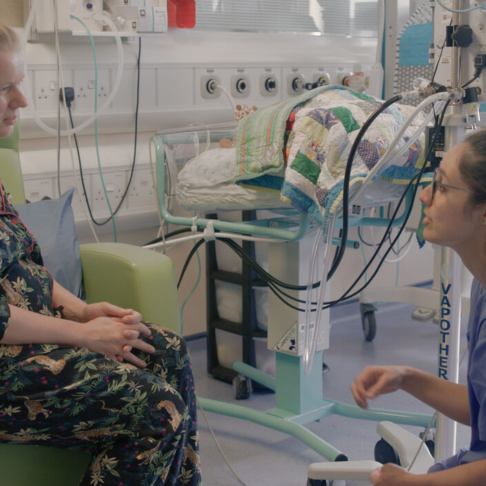 Nurse kneeling down while talking to parent sitting in a hospital chair