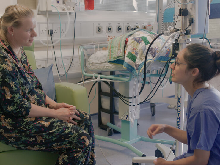 Nurse kneeling down while talking to parent sitting in a hospital chair
