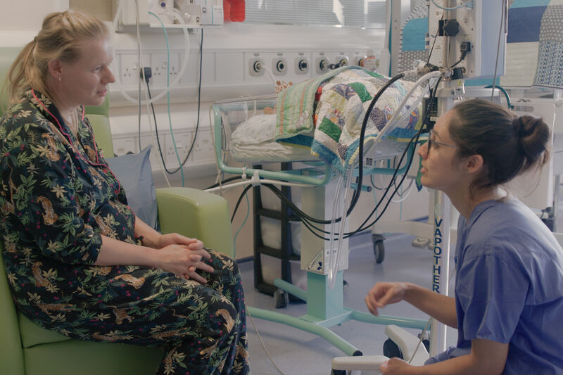 Nurse kneeling down while talking to parent sitting in a hospital chair