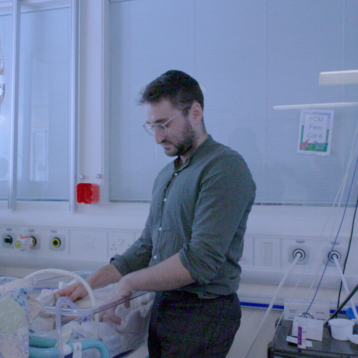 Parent touching their sleeping baby in a hospital room.