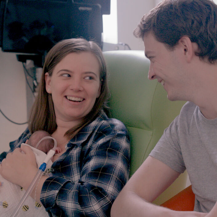 Two parents looking at each other and smiling while their baby rests on the mother's chest