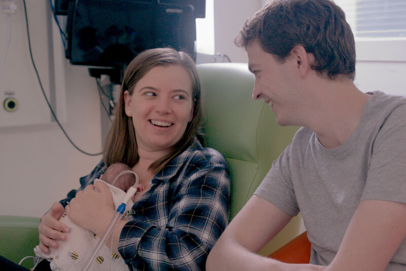 Two parents looking at each other and smiling while their baby rests on the mother's chest