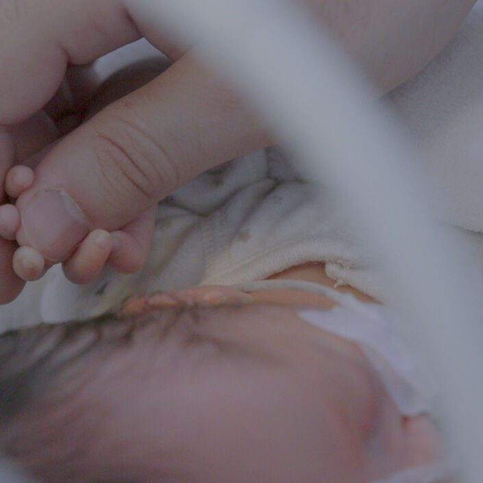 Baby lying down holding onto their parent's thumb.