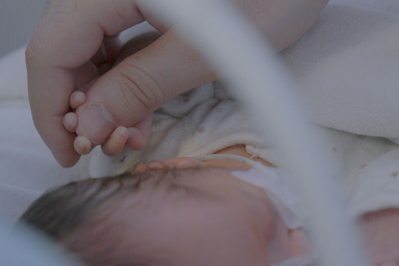 Baby lying down holding onto their parent's thumb.