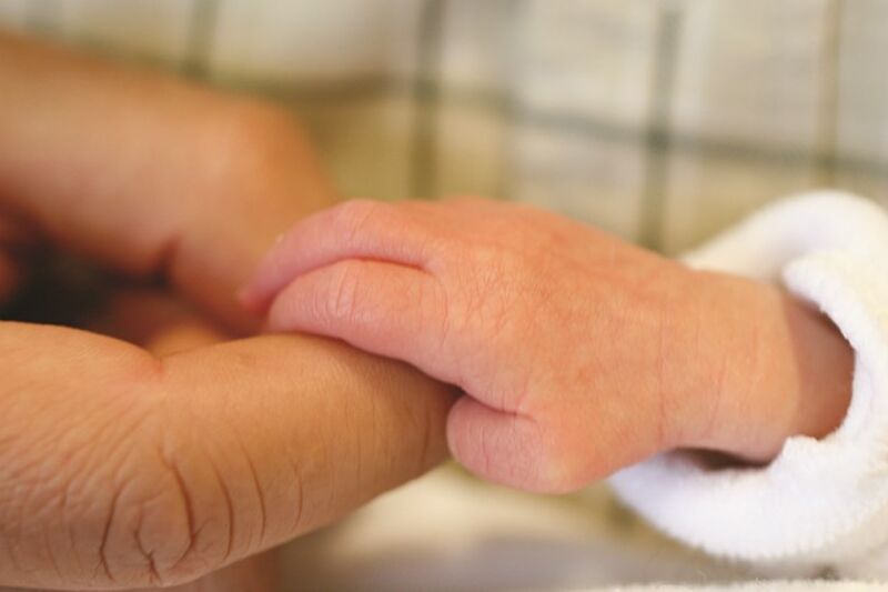 A tiny baby hand grasping onto its parent's index finger.