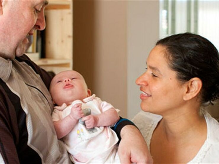 Dad holding a baby smiling looking down at baby with mum alongside also looking at the baby