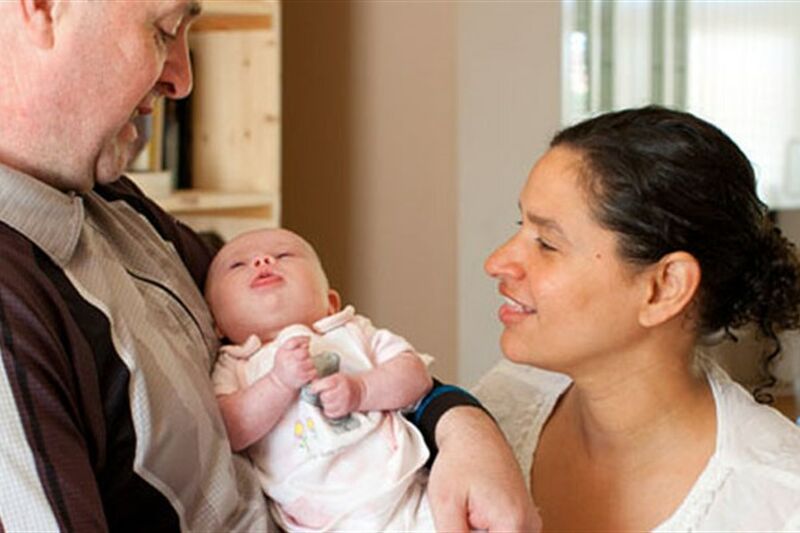 Dad holding a baby smiling looking down at baby with mum alongside also looking at the baby