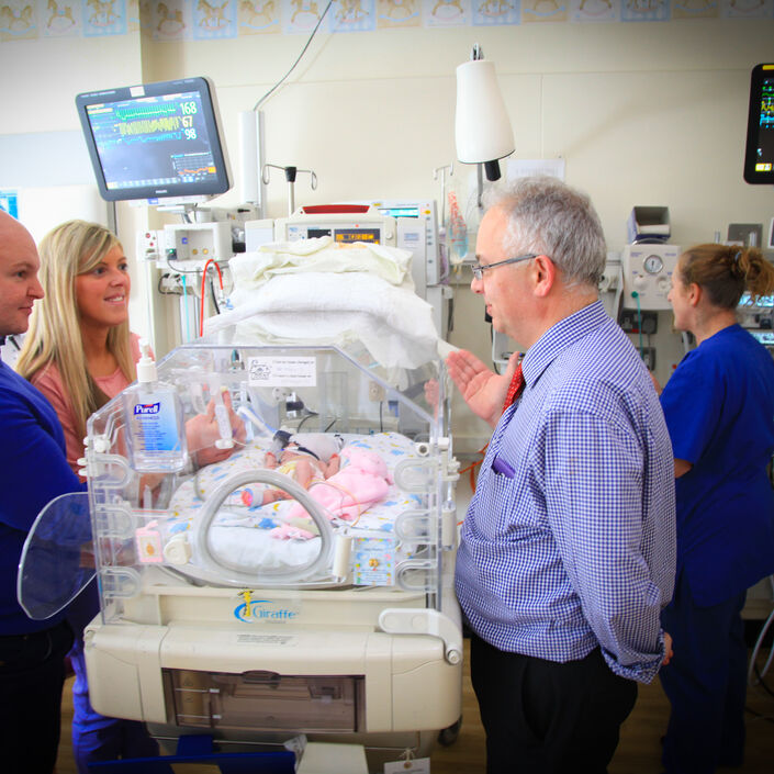 Parents standing on one side of an incubator with their baby inside talking to a doctor on the other side of the incubator