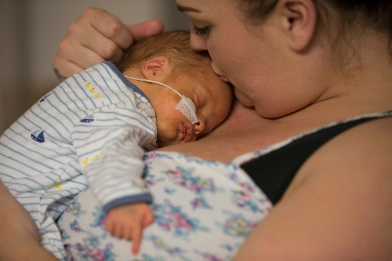 Mum holding baby on her chest while kissing baby's forehead