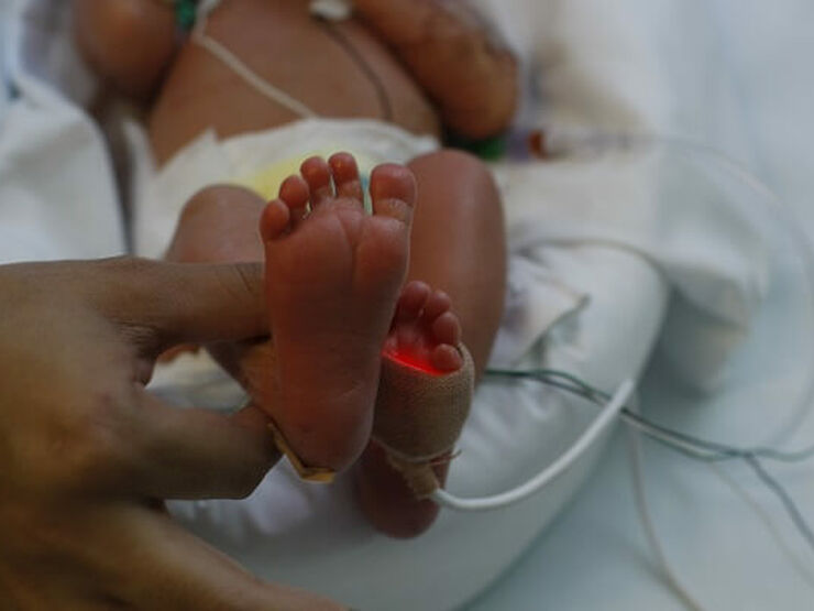 Parent holding premature baby's foot in hospital
