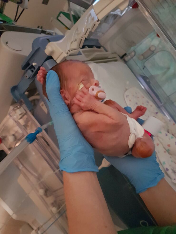 Elizabeth, a baby, being held with gloves near incubator