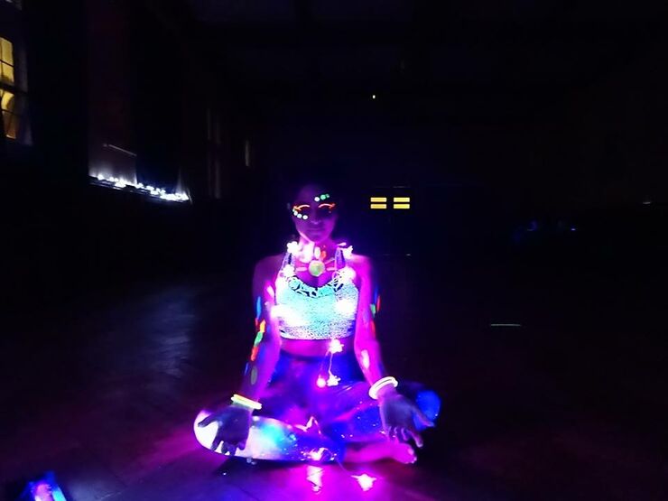 lady sitting in cross legged yoga position with lights and UV glow sticks
