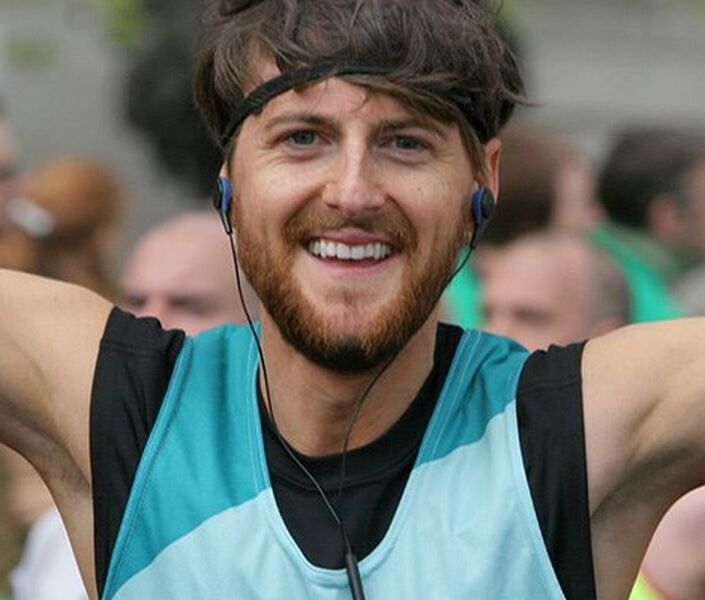 Head shot of man running celebrating with arms in the air at an event wearing a Bliss running vest