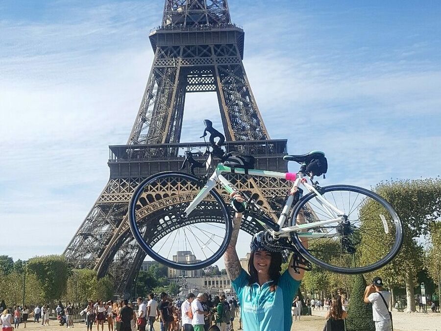 Bliss rider holding her bike above her head in front of the eiffel tower